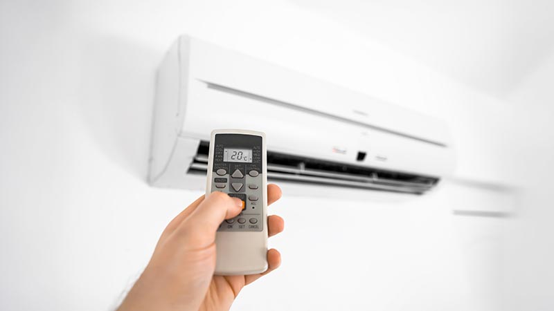 Mão com comando a ligar um aparelho de ar condicionado